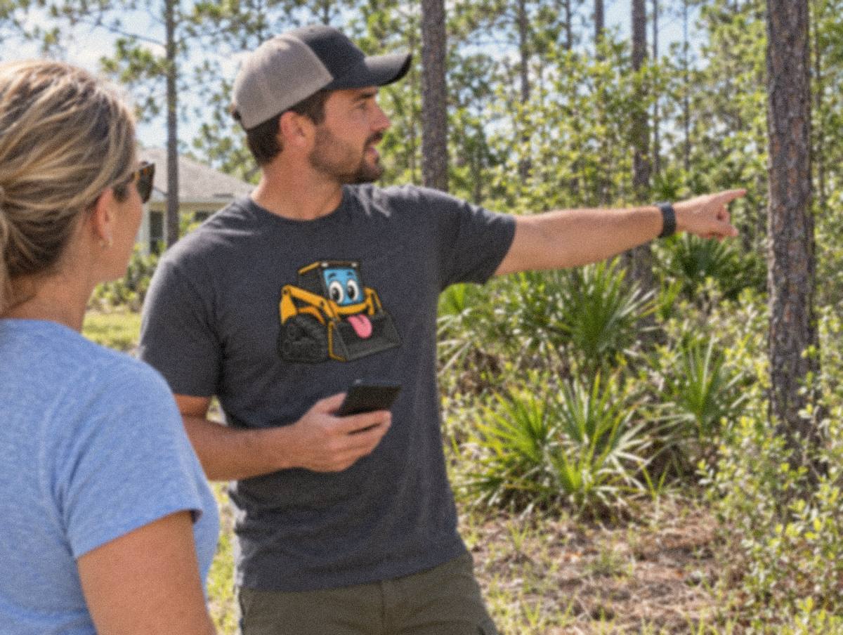 Illustration of a man in a skid steer mascot shirt pointing across a wooded lot of pines and palmetto while talking with a woman